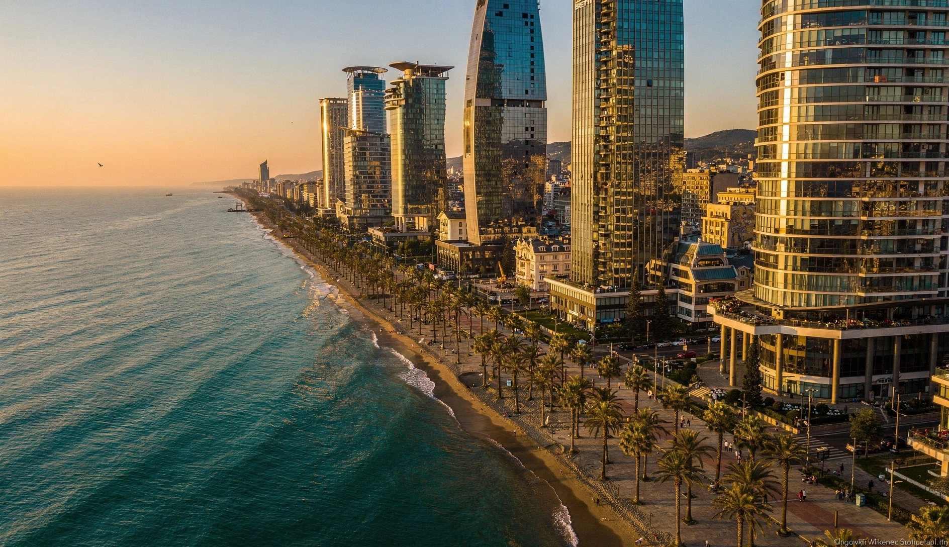 Aerial view of Batumi coastline at golden hour with modern towers and palm-lined boulevard