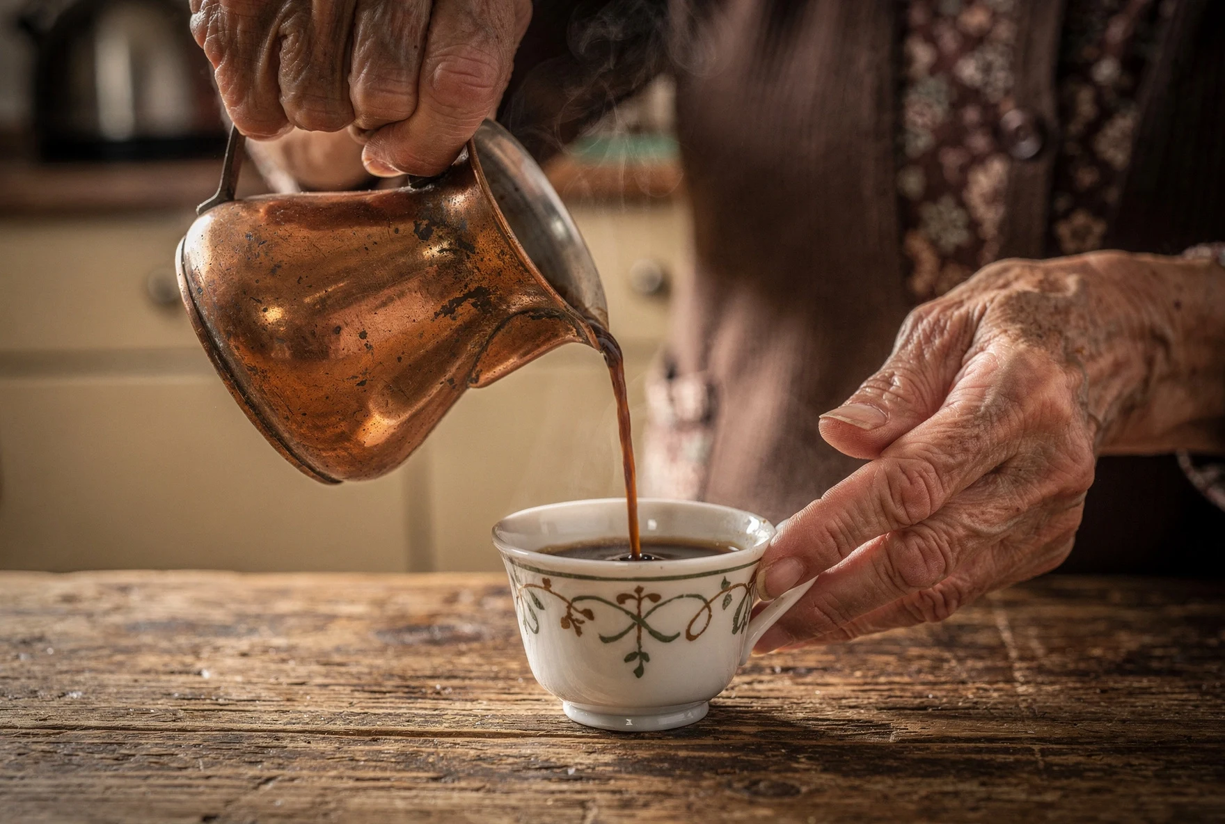 Elderly hands pouring Turkish coffee from a copper cezve into a decorated cup
