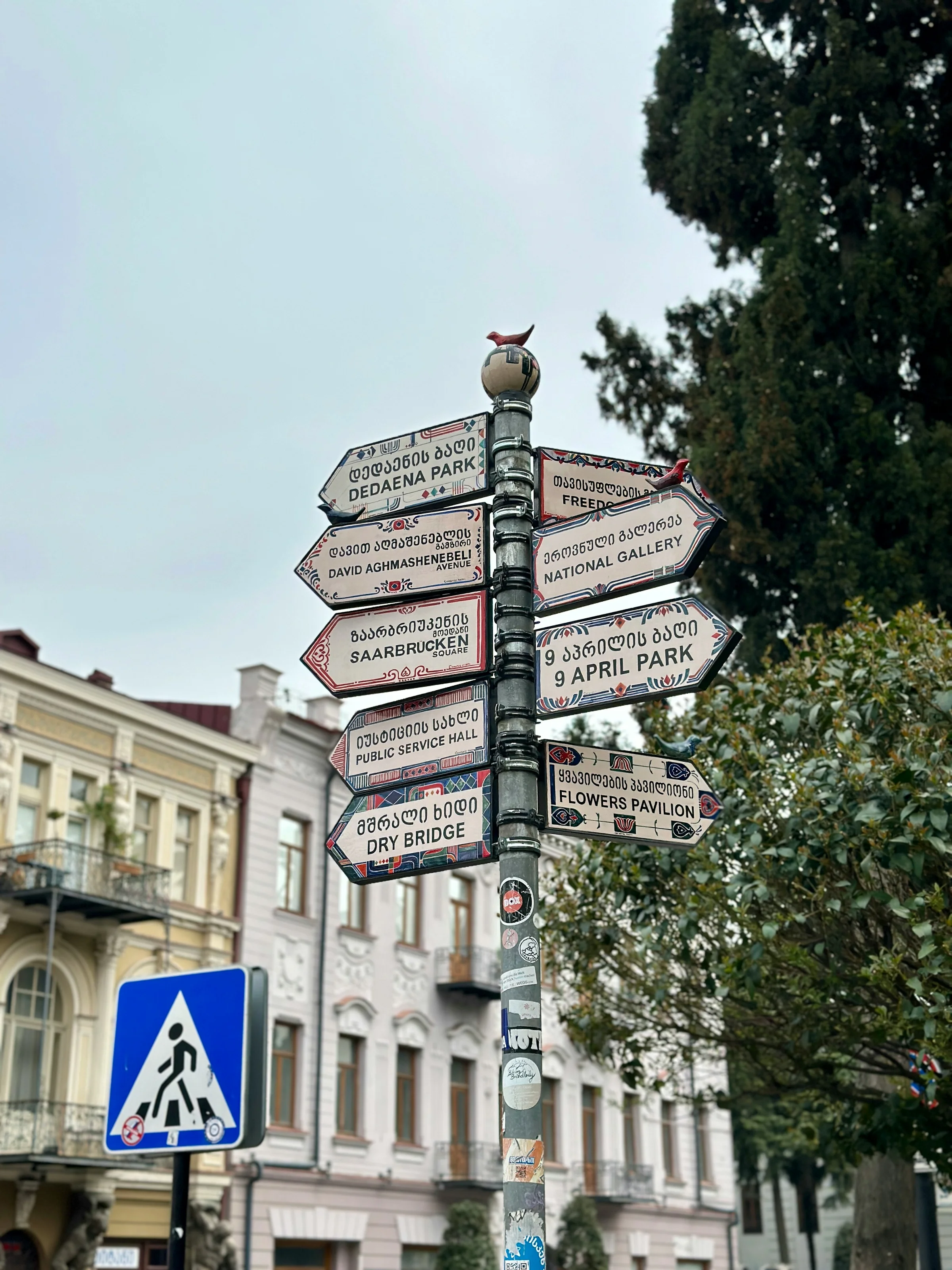 Directional signpost in Tbilisi showing Georgian and English text, pointing to landmarks like Freedom Square and Dry Bridge