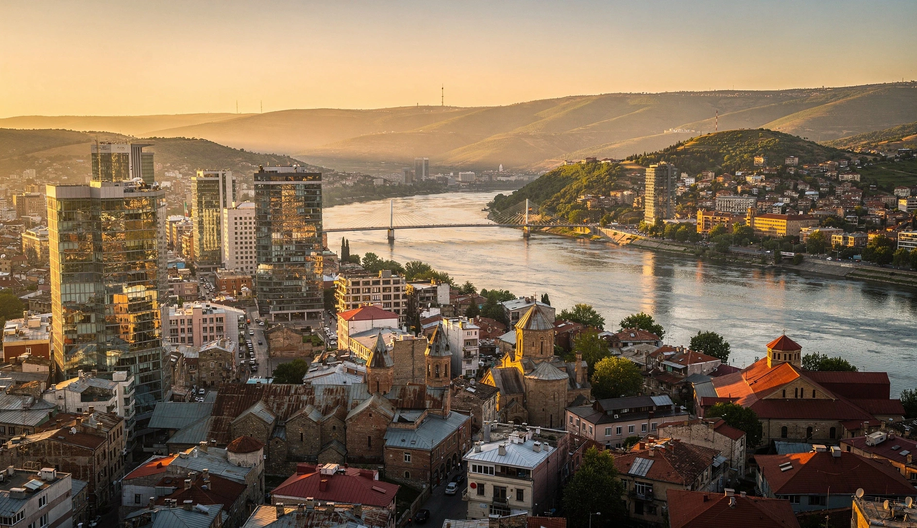 Aerial view of Tbilisi cityscape at golden hour with the Kura River and mix of modern and historic architecture