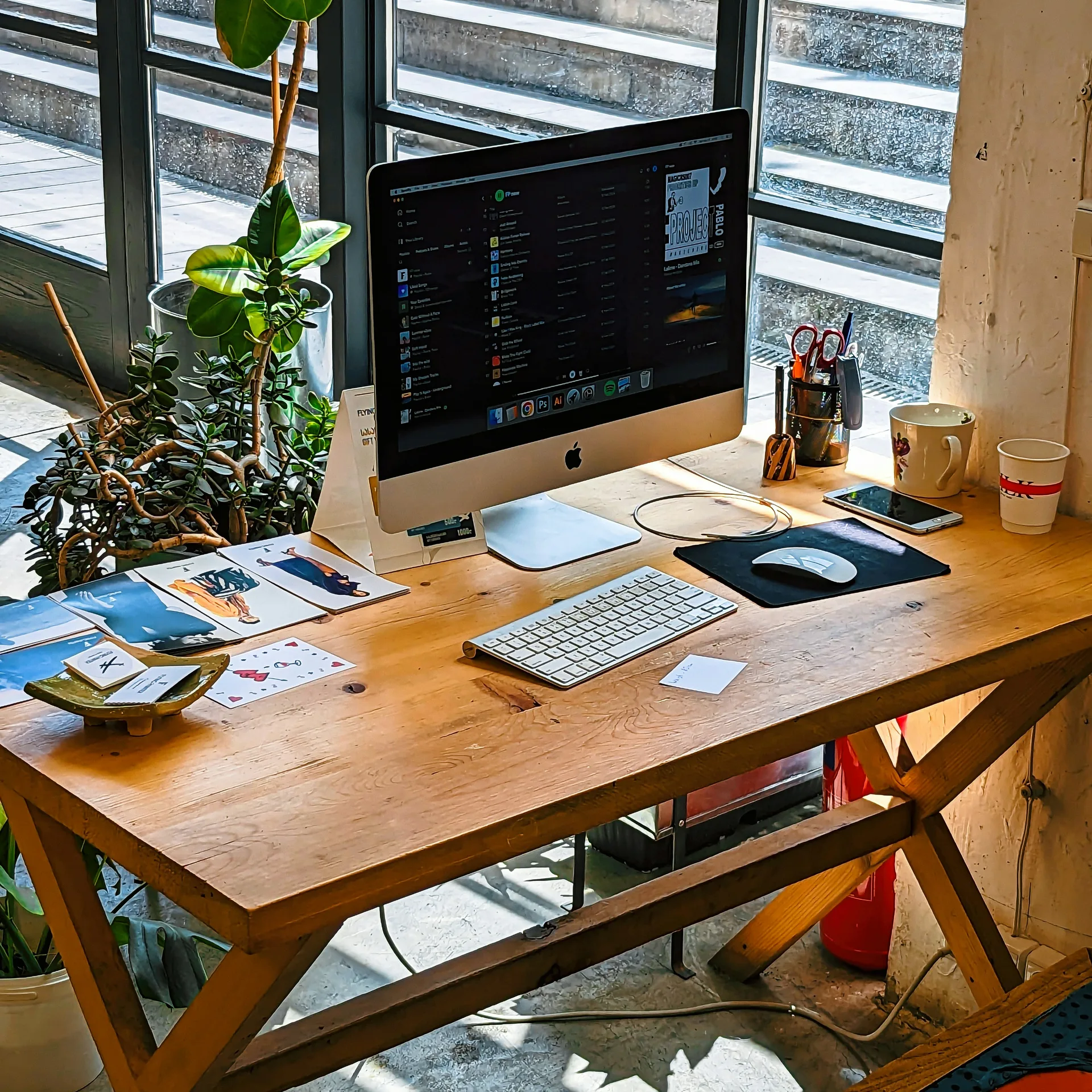 A creative workspace with a computer and plants by large industrial windows in Tbilisi